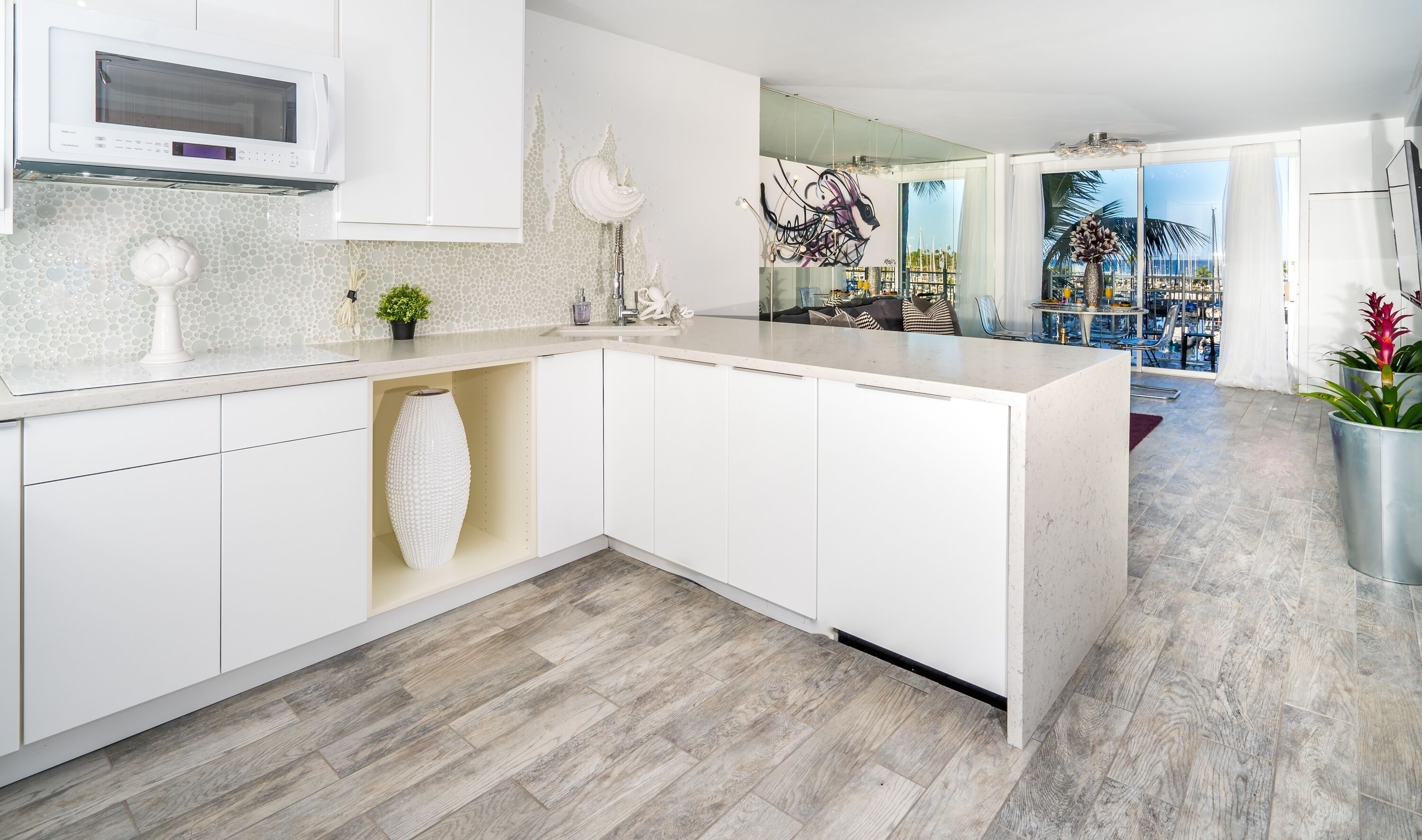 A modern kitchen with white cabinetry, a built-in microwave, and a large island with a vase and plant.