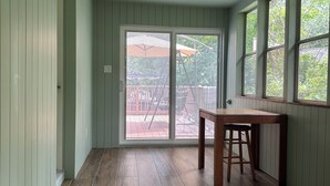 Une pièce dotée d’un plancher en bois, d’une table avec un tabouret et de grandes fenêtres donnant sur l’extérieur.