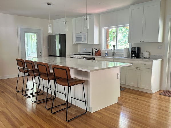 A modern kitchen with a large island, bar stools, stainless steel appliances, and white cabinetry.