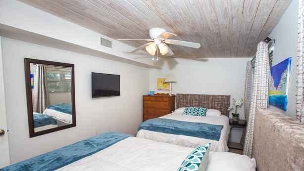 Ein Schlafzimmer mit zwei Betten, einem Deckenventilator, einem Fernseher und Kunstwerken an der Wand.