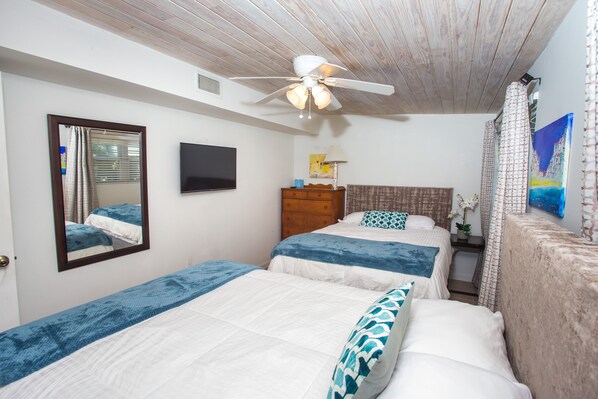 Ein Schlafzimmer mit zwei Betten, einem Deckenventilator, einem Fernseher und Kunstwerken an der Wand.