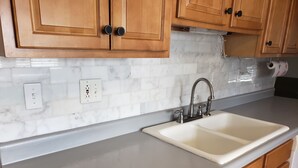 Eine Küche mit Holdekor-Schränken, einer weißen Marmor-Spritzschutzwand und einer Spüle mit moderner Armatur.