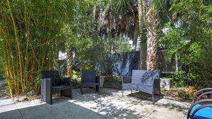 Ein Außenbereich mit einer Terrasse, zwei Stühlen, einem Tisch und einer großen Bambuspflanze.