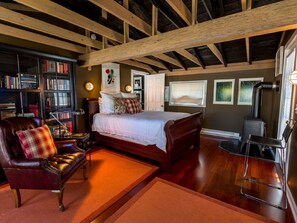 Une chambre confortable avec un grand lit, un fauteuil en cuir, une bibliothèque et une cheminée.