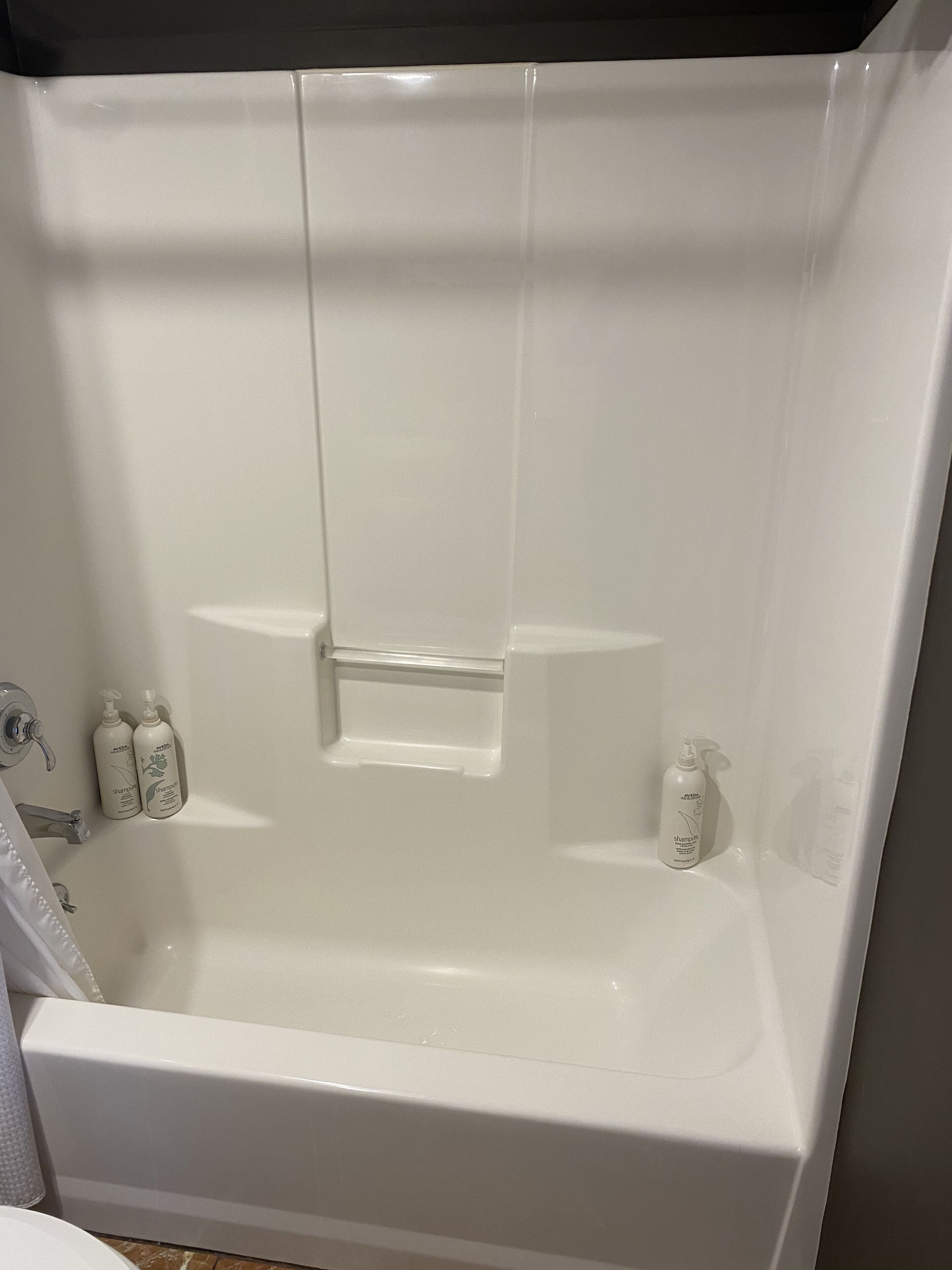 Una bañera blanca con dos botellas de champú a la izquierda.
