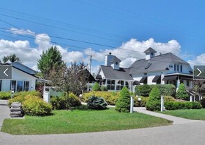 Une maison à deux étages avec une grande pelouse devant, une allée et un jardin bien entretenu.