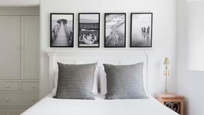 A bedroom with a bed, two pillows, a bedside table with a lamp, and four framed pictures on the wall.