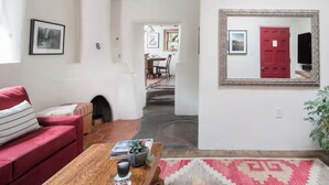 A living room with a red sofa, a wooden coffee table, and a rug. There is a framed mirror on the wall and a door with a red handle.