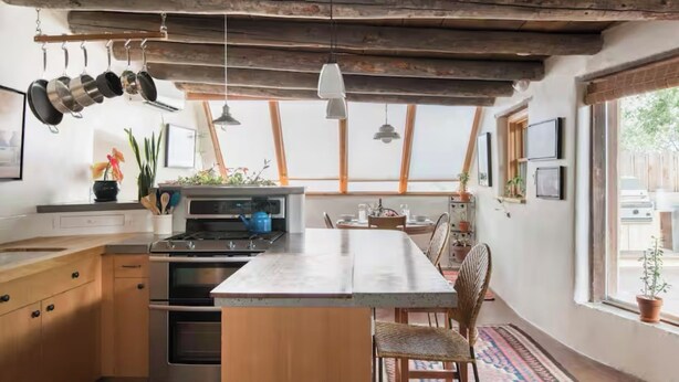 A kitchen with wooden cabinets, a central island, hanging pots, and a view of the outdoors.