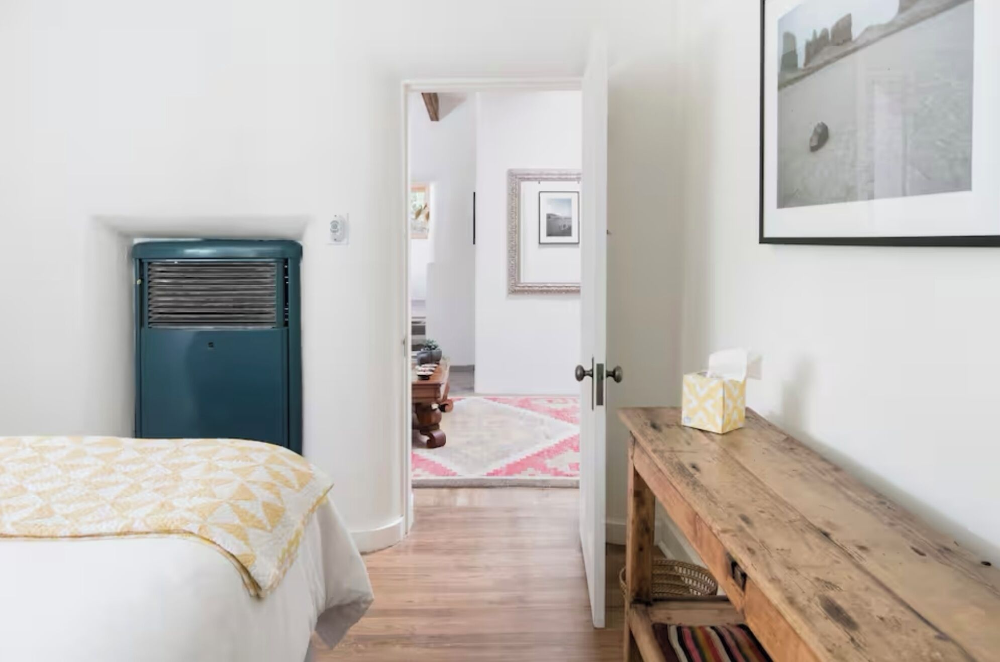 Un dormitori amb un llit, una banca de fusta, un radiador i una porta que dona a una altra habitació.