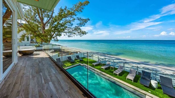 A poolside area with a view of the ocean, lounge chairs, and a glass railing.