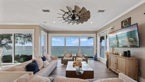 A spacious living room with a large TV, comfortable seating, and a ceiling fan.
