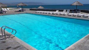 Una piscina con agua azul cristalina, rodeada de sillas de descanso blancas y sombrillas de paja.