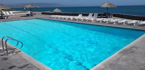 Relax by the pool surrounded by lounge chairs and thatched umbrellas.