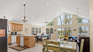 A spacious kitchen with wooden cabinets, a dining area with a table and chairs, and large windows offering views of the outdoors. - Vast Lakefront Home with Rec Room and Fire Pit (Pullman)