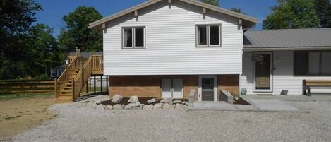 A two-story house with a front porch, a wooden staircase, and a gravel driveway.