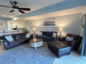 Uma sala de estar com um sofá de couro escuro, uma mesa de centro redonda e um ventilador de teto.