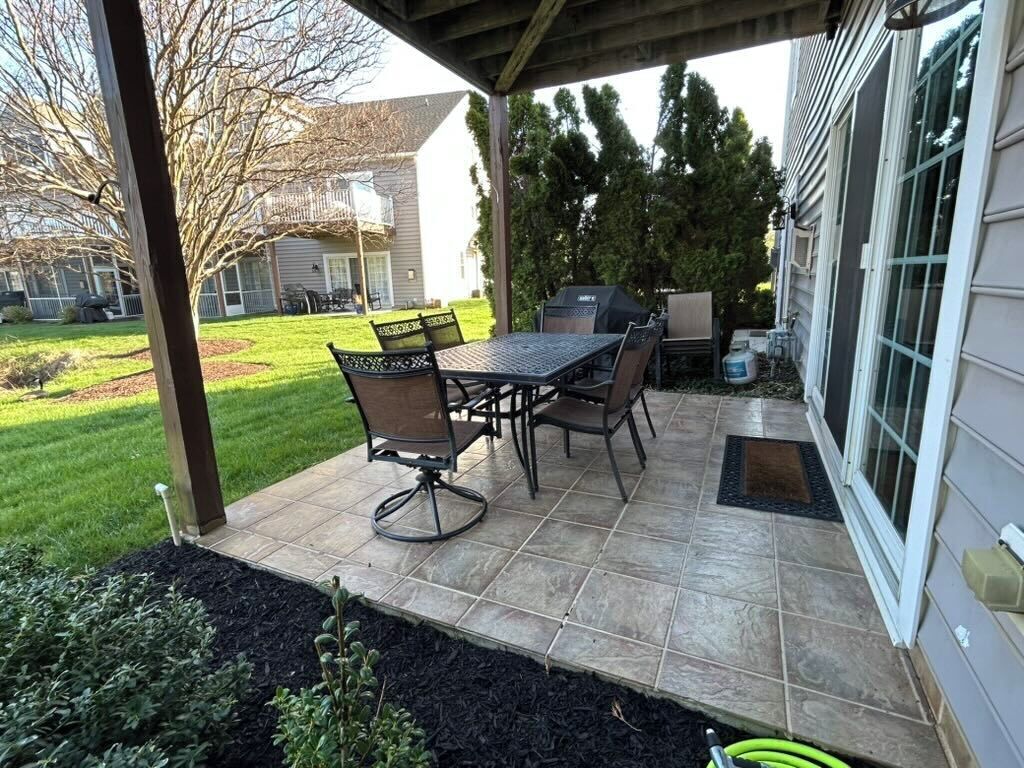 An outdoor patio with a table and chairs, a grill, and a covered area.