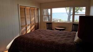 Une chambre à coucher avec un lit, une fenêtre donnant sur l’eau, ainsi qu’une petite table et une chaise.