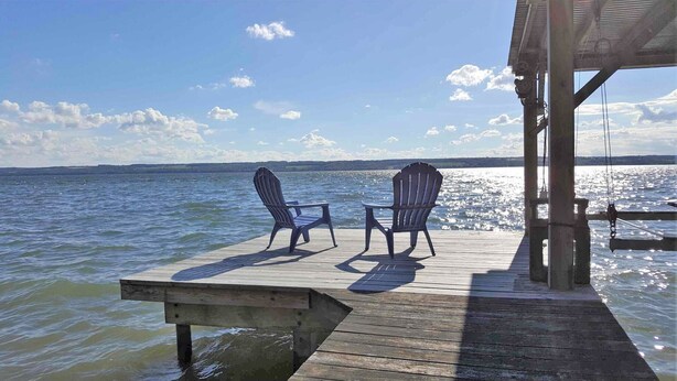 Une jetée en bois avec deux chaises Adirondack donnant sur une étendue d’eau calme.