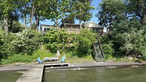 Une maison avec un quai et une petite jetée, entourée d’arbres et bordée par un plan d’eau.