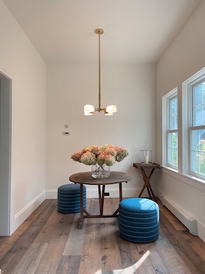 A dining area with a wooden table, blue ottomans, a vase of flowers, and a chandelier.