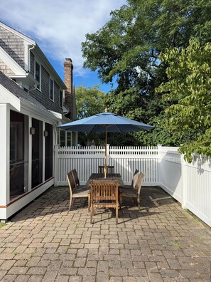A patio with a table and chairs, a blue umbrella, and a white picket fence.