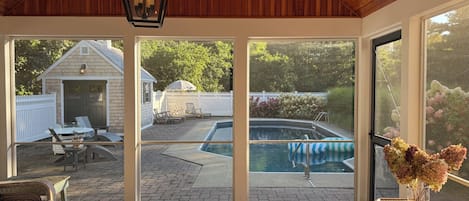 A covered patio with a pool, outdoor furniture, and a view of a backyard.