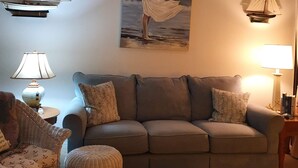 Ett vardagsrum med en soffa, två fåtöljer, ett soffbord och segelbåtar som hänger på väggen.