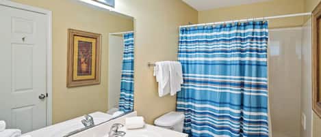 A bathroom with a white sink, mirror, and toilet. There are towels on the sink and a shower curtain.