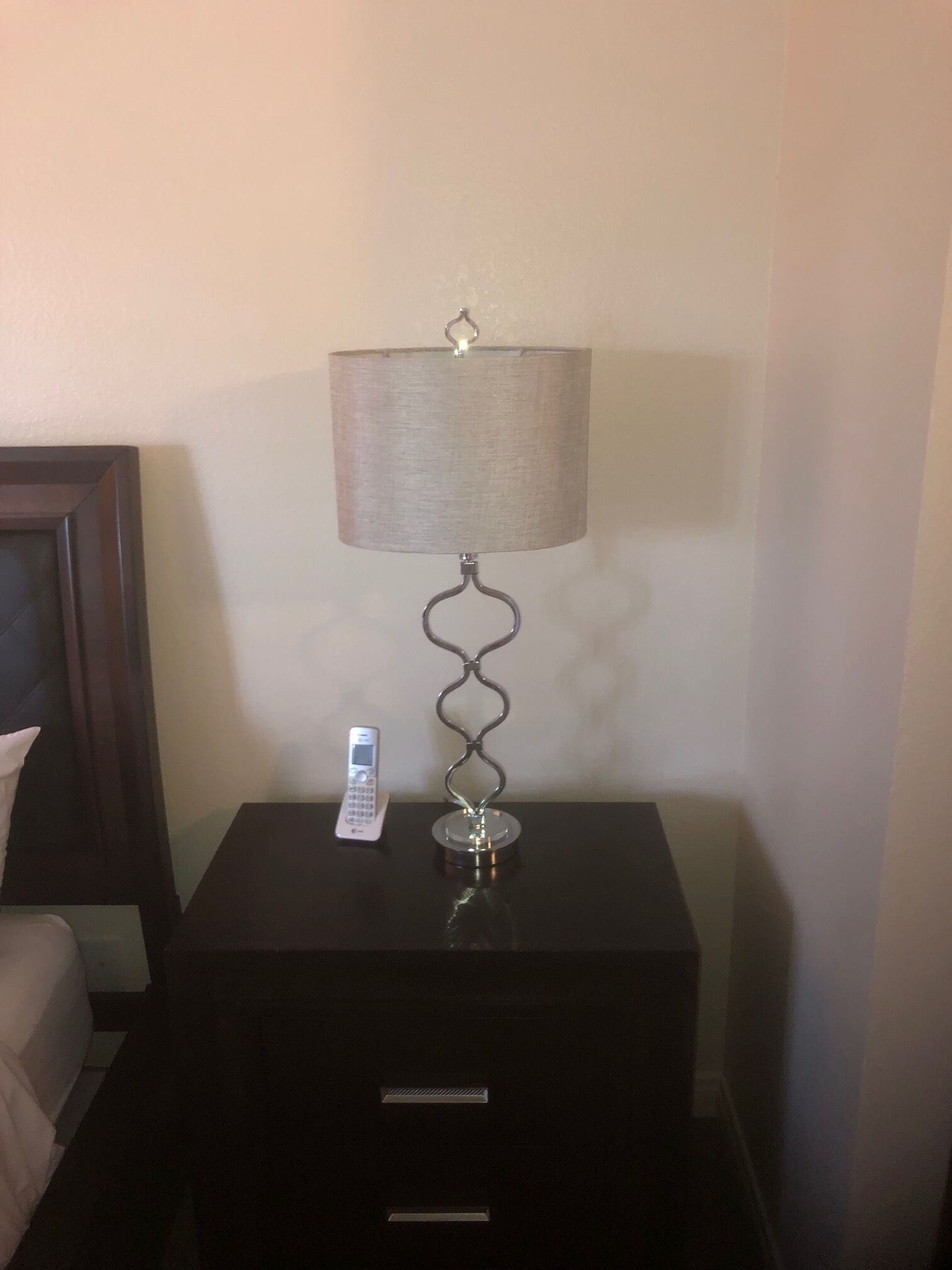 A bedside table with a lamp, a remote control, and a drawer.