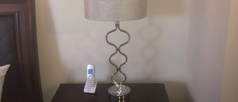 A bedside table with a lamp, a remote control, and a drawer.