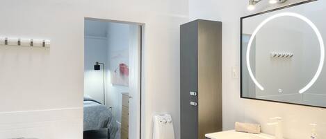 Ein modernes Badezimmer mit einem weißen Waschbecken, einem Spiegel mit runder Beleuchtung und einem Handtuchspender.