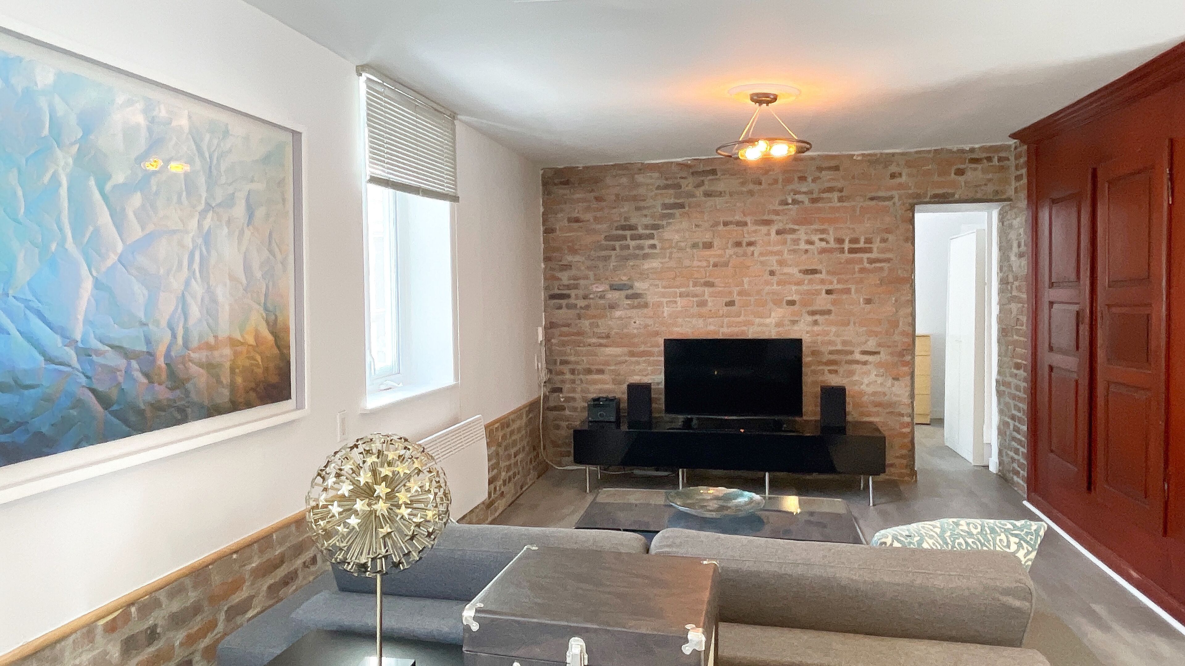A living room with a brick wall, a flat-screen TV, and a large abstract painting.