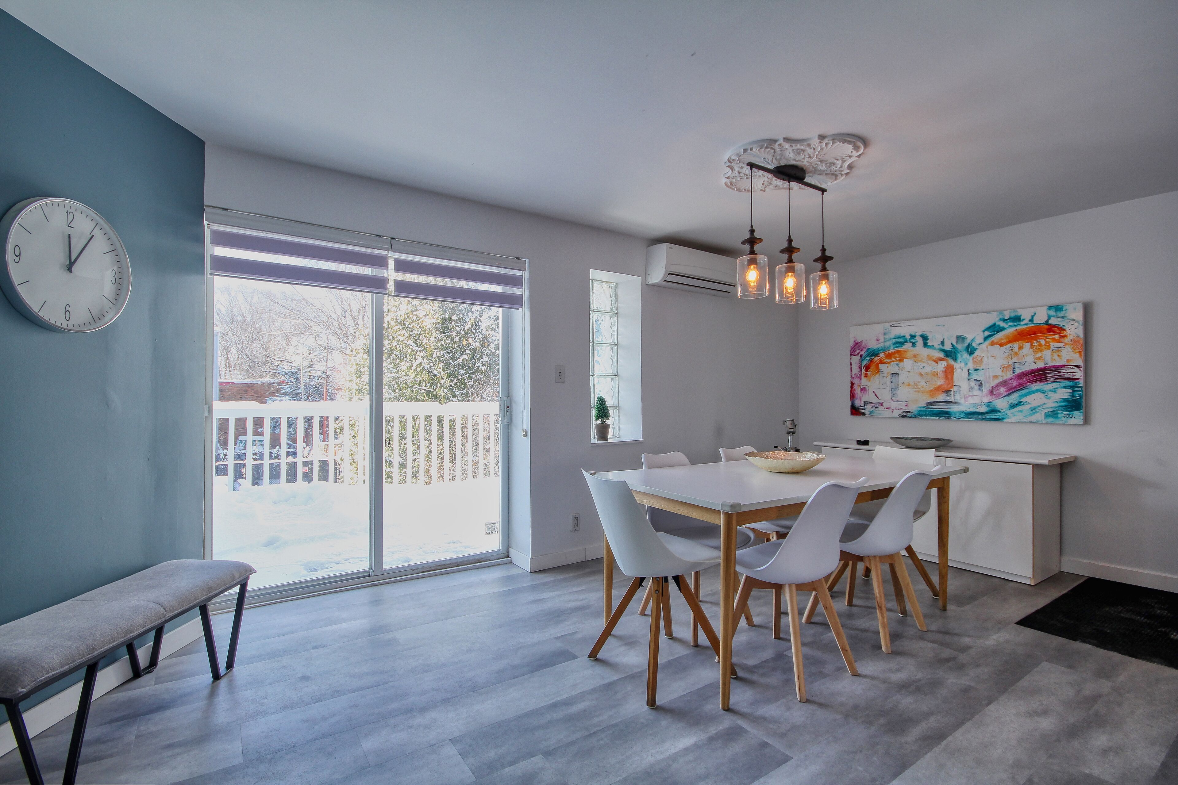 Un espace repas moderne avec une grande table, des chaises blanches et un banc.
