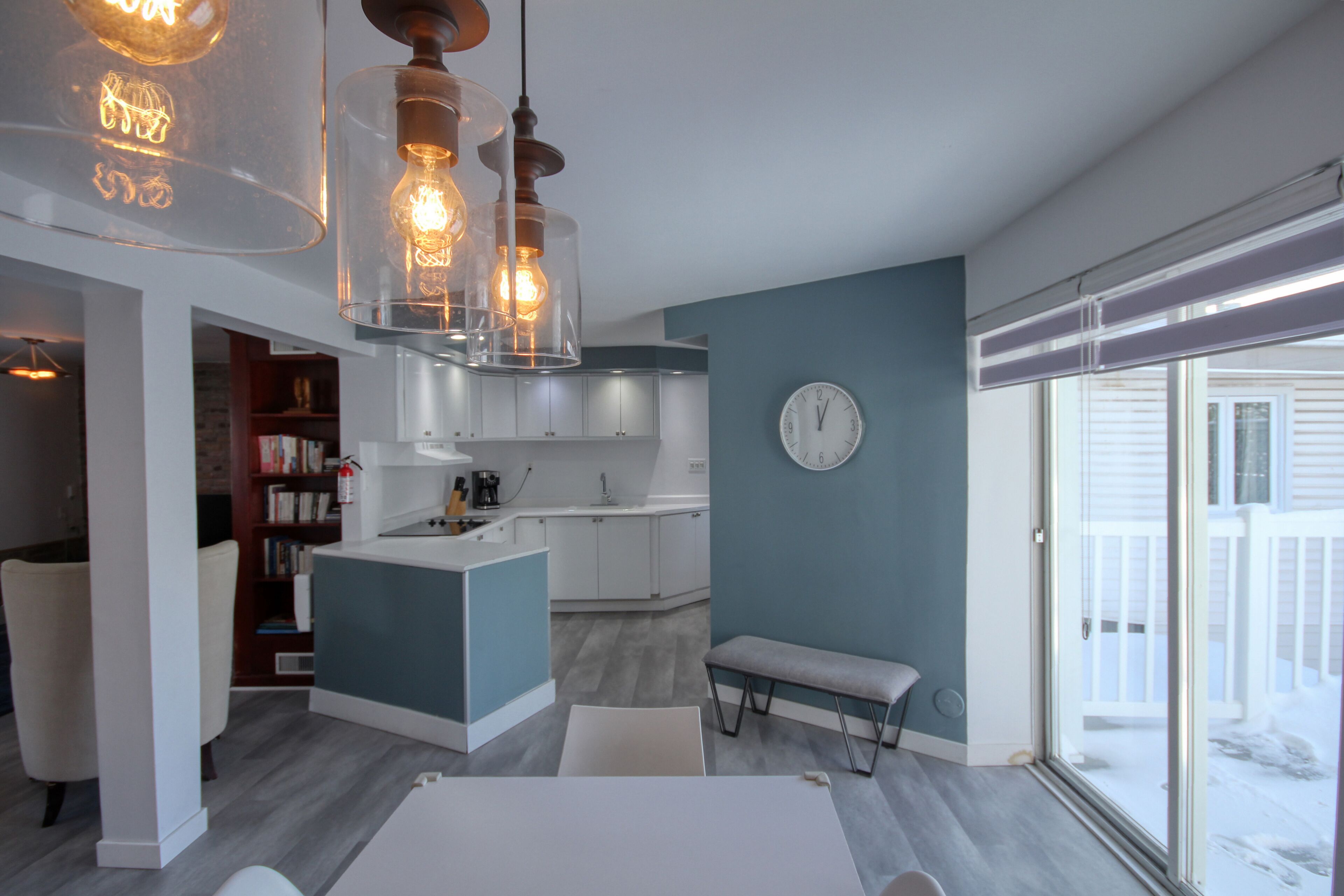 Une cuisine moderne dotée d’un îlot central, de luminaires suspendus et d’une grande fenêtre offrant une vue sur l’extérieur.