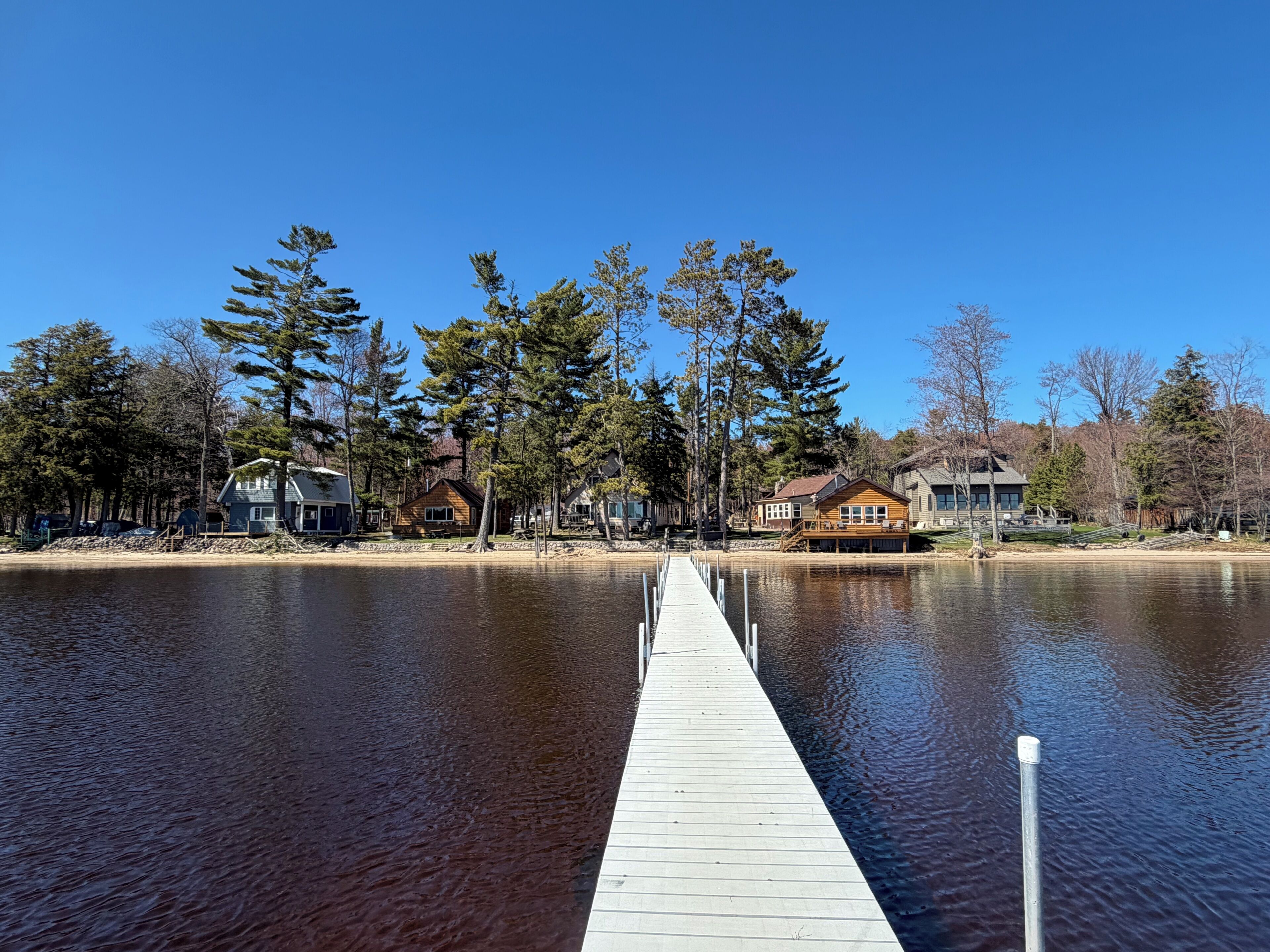 A wooden dock extending into a calm lake, surrounded by houses with visible decks and waterfront views.