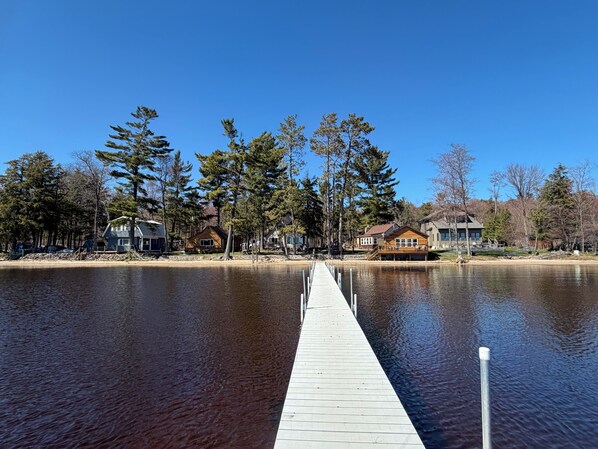 A wooden dock extending into a calm lake, surrounded by houses with visible decks and waterfront views. - Spacious 2 Bedroom Cabin @ Northwoods Resort (AuTrain)