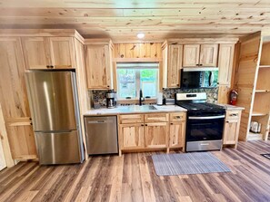 A kitchen with wooden cabinets, stainless steel appliances, a window, and a stone backsplash.