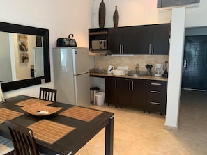 A compact kitchen with dark cabinets, a stainless steel sink, and a refrigerator. There is a dining table with placemats and chairs.