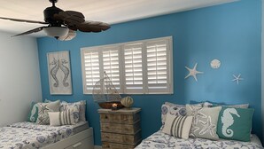 Quarto com duas camas, uma cômoda e um ventilador de teto.