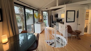 Eine moderne Küche mit weißen Schränken, einer Mikrowelle und einem Spülbecken. Es gibt einen Essbereich mit einem Glastisch und Stühlen, sowie eine Treppe, die zu einer oberen Ebene führt.