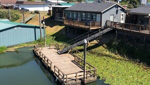 Une jetée s’avançant dans une étendue d’eau où flottent des nénuphars, reliée à un bâtiment doté d’un balcon.