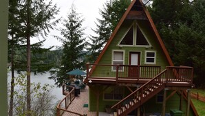 Une cabane dotée d’une terrasse, d’un escalier et offrant une vue sur un lac entouré d’arbres.