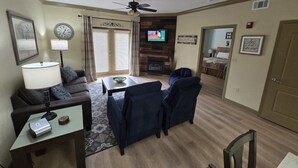 Una sala de estar con sofá, sillas, una mesa de centro, lámpara, reloj, televisor y chimenea.