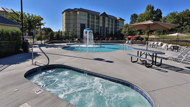 Zona de piscina de hotel con jacuzzi, sillones de descanso y sombrillas.
