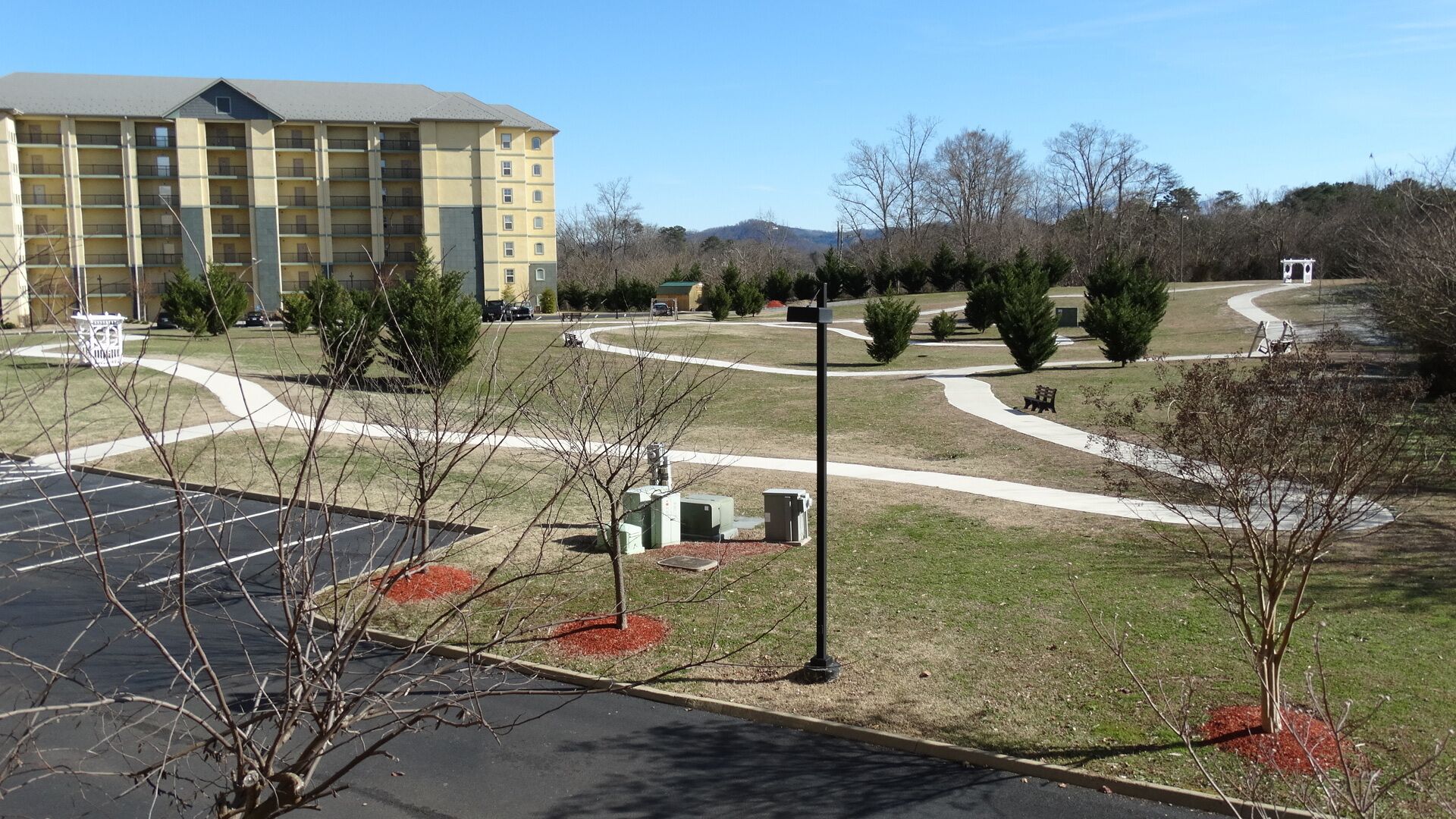 A hotel with a parking lot, a landscaped area with trees, and a building with multiple floors.