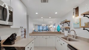 Une cuisine moderne avec des meubles blancs, une cuisinière en acier inoxydable et un lave-vaisselle. Une grande fenêtre offre une vue sur l’extérieur.
