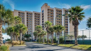 Un hôtel à plusieurs étages doté d’une cour intérieure, entouré de palmiers et d’un parking délimité par une clôture.
