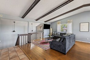 Un vaste salon comprenant une table à manger en bois, un canapé gris et un escalier menant à l’étage supérieur.